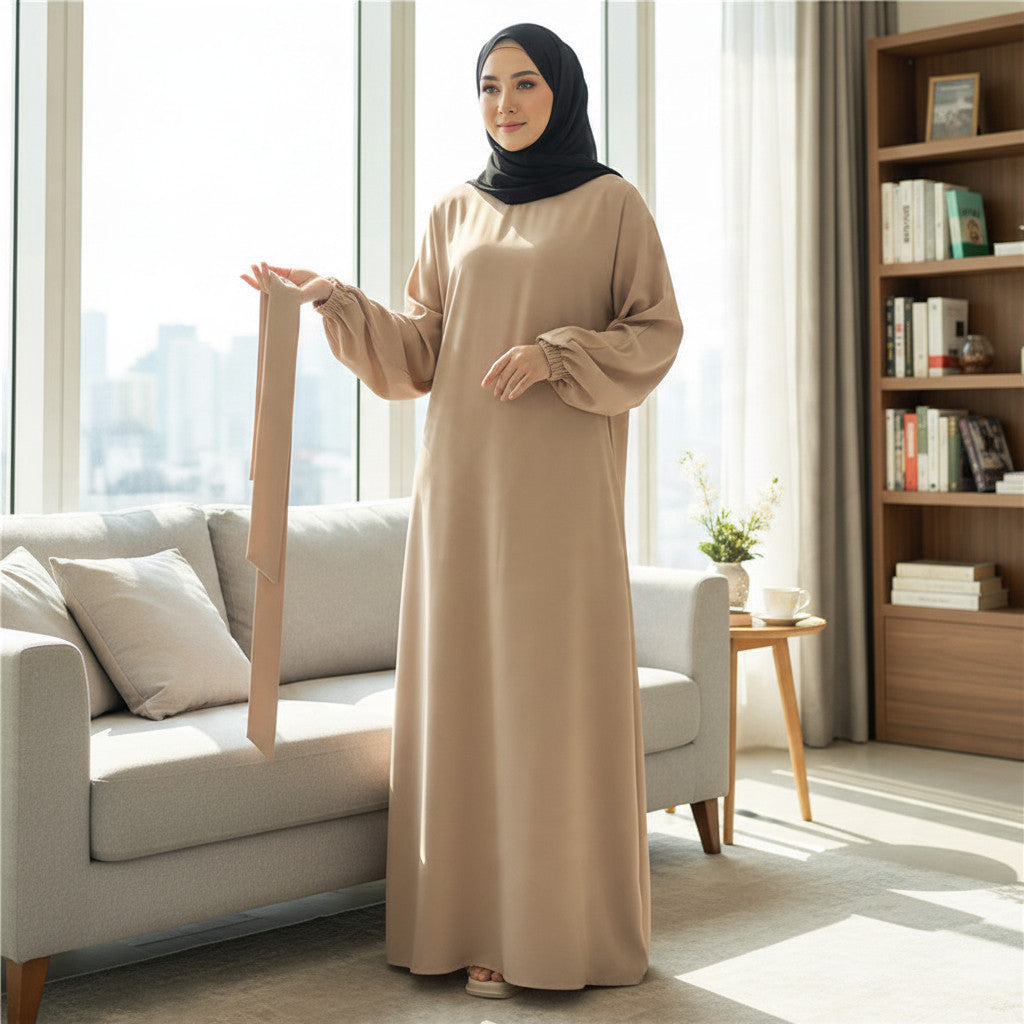 BelleNoor beige abaya with long balloon sleeves and elastic cuffs worn by a woman in a bright, modern living room.