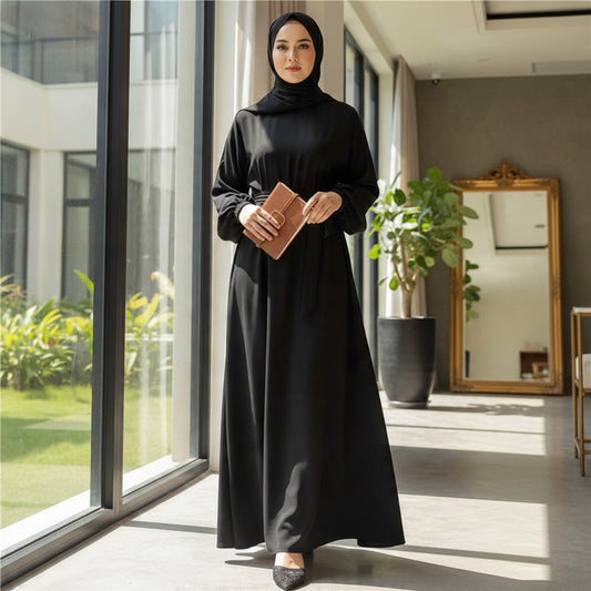 BelleNoor black maxi abaya dress with tie-waist and elastic cuffs worn by a woman in a bright, modern interior.