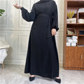 BelleNoor black Nida fabric abaya with long sleeves and a waist tie, worn by a model in a bright indoor setting.
