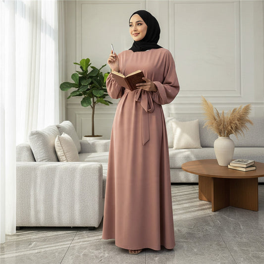 Woman wearing a dusty rose BelleNoor Nida abaya with a black hijab, standing in a bright, modern living room.