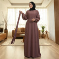 BelleNoor purple Nida abaya with long sleeves and a matching tie belt, worn by a woman in a modern living room.