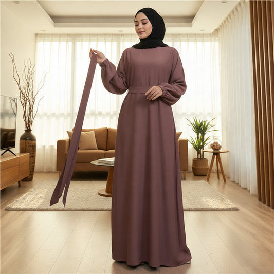 BelleNoor purple Nida abaya with long sleeves and a matching tie belt, worn by a woman in a modern living room.