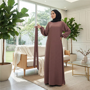 Model wearing a purple BelleNoor Nida fabric abaya with long sleeves and a matching tie belt in a bright living room.
