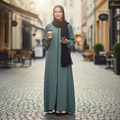 BelleNoor sage green front-zip abaya with black hijab worn by a woman holding a coffee cup on a city street