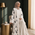 BelleNoor white abaya with black and grey floral print, wide sleeves, and matching hijab worn by a seated woman.
